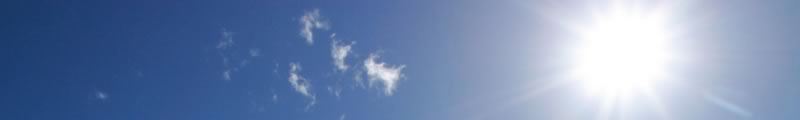 Sun shining in a blue sky with some whisps of white clouds visible.